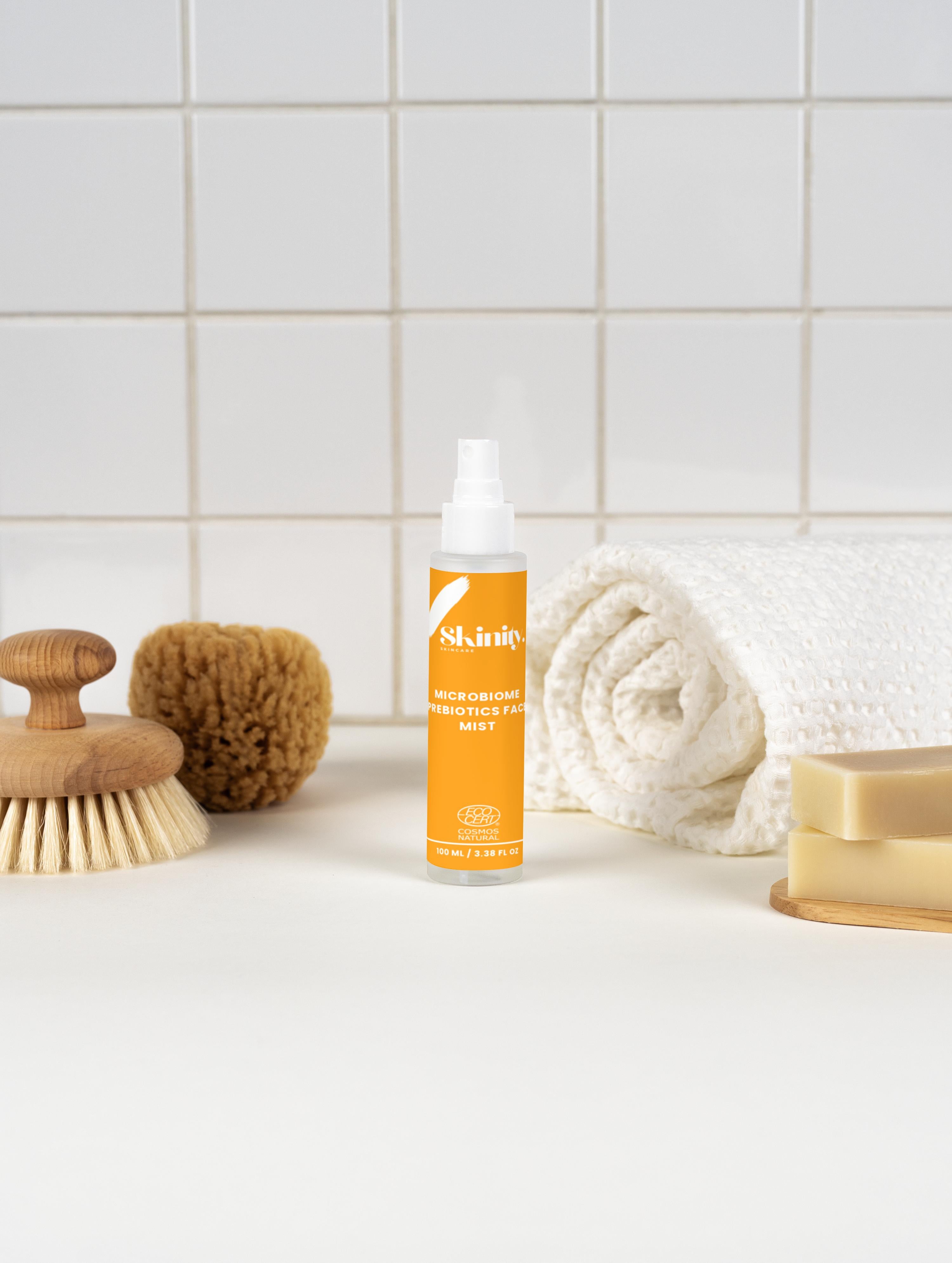 Microbiome Prebiotics Face Mist on a flat surface with towels and natural brushes for skincare.