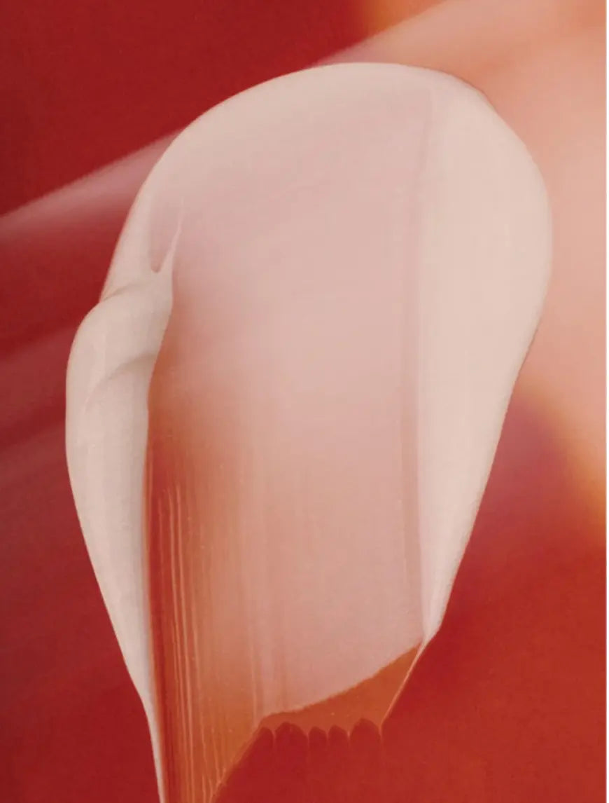 A close-up of a smooth, rounded pale pink product shape against a warm red-orange background.