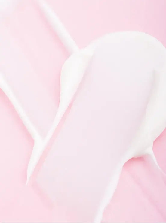 A close-up of a thick, creamy white cosmetic or lotion texture spread across a soft pink background.