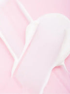 A close-up of a thick, creamy white cosmetic or lotion texture spread across a soft pink background.