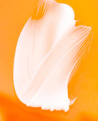 A thick, creamy white cosmetic or skincare product swatch, likely a cream or lotion, swirled on a vibrant orange background.