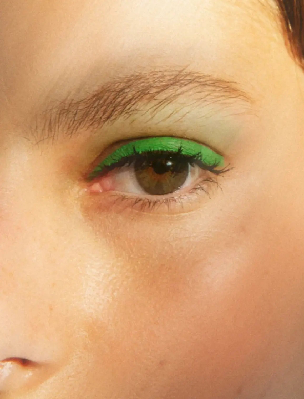 Close-up of a person's eye wearing a bright neon green eyeshadow and black eyeliner.
