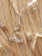 Close-up of light golden-blonde hair with water droplets and a glossy sheen, showing texture and shine in macro detail.