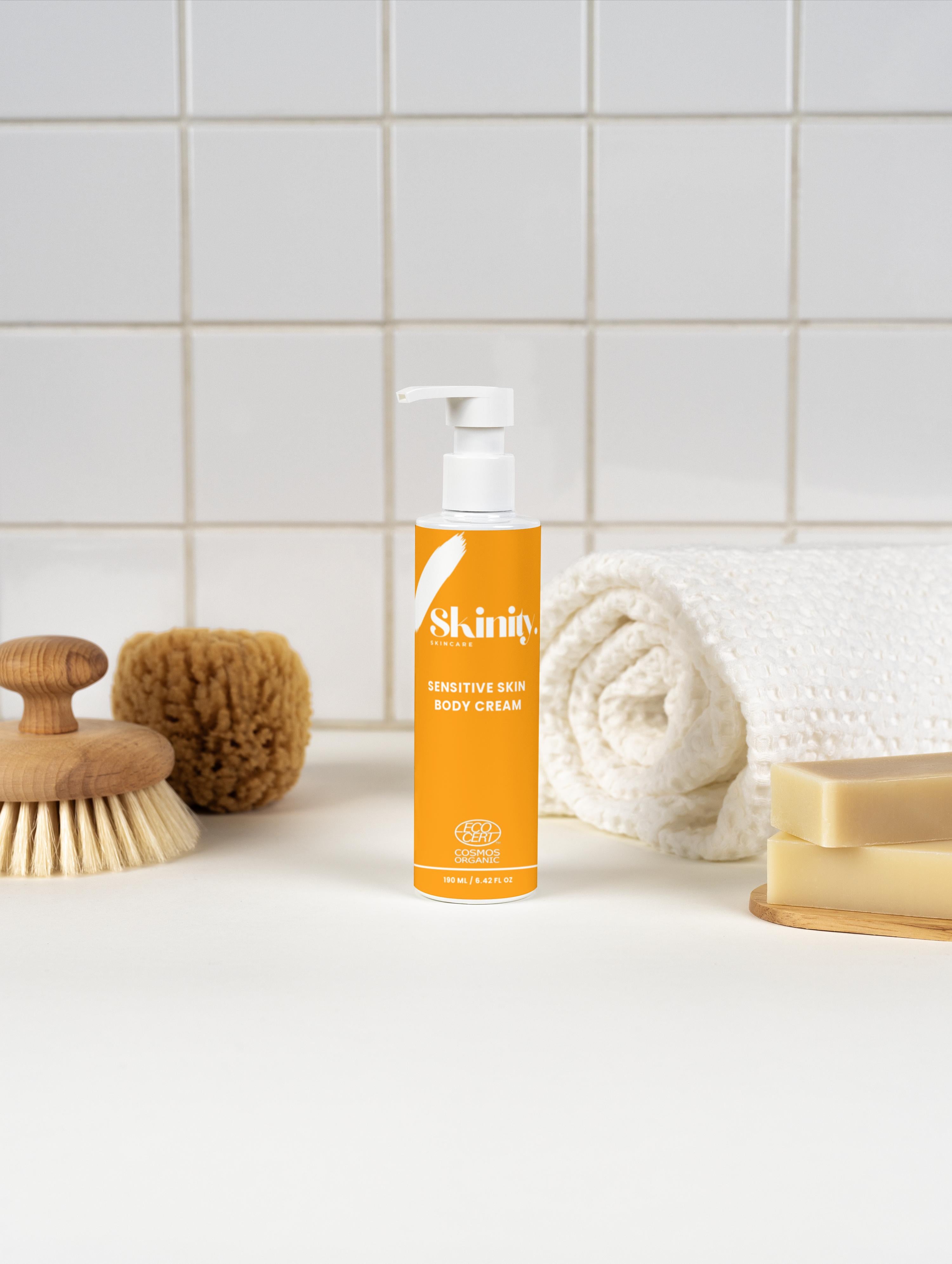 Sensitive Skin Body Cream Vegan in a pump bottle with natural brushes and towels in a serene setting.