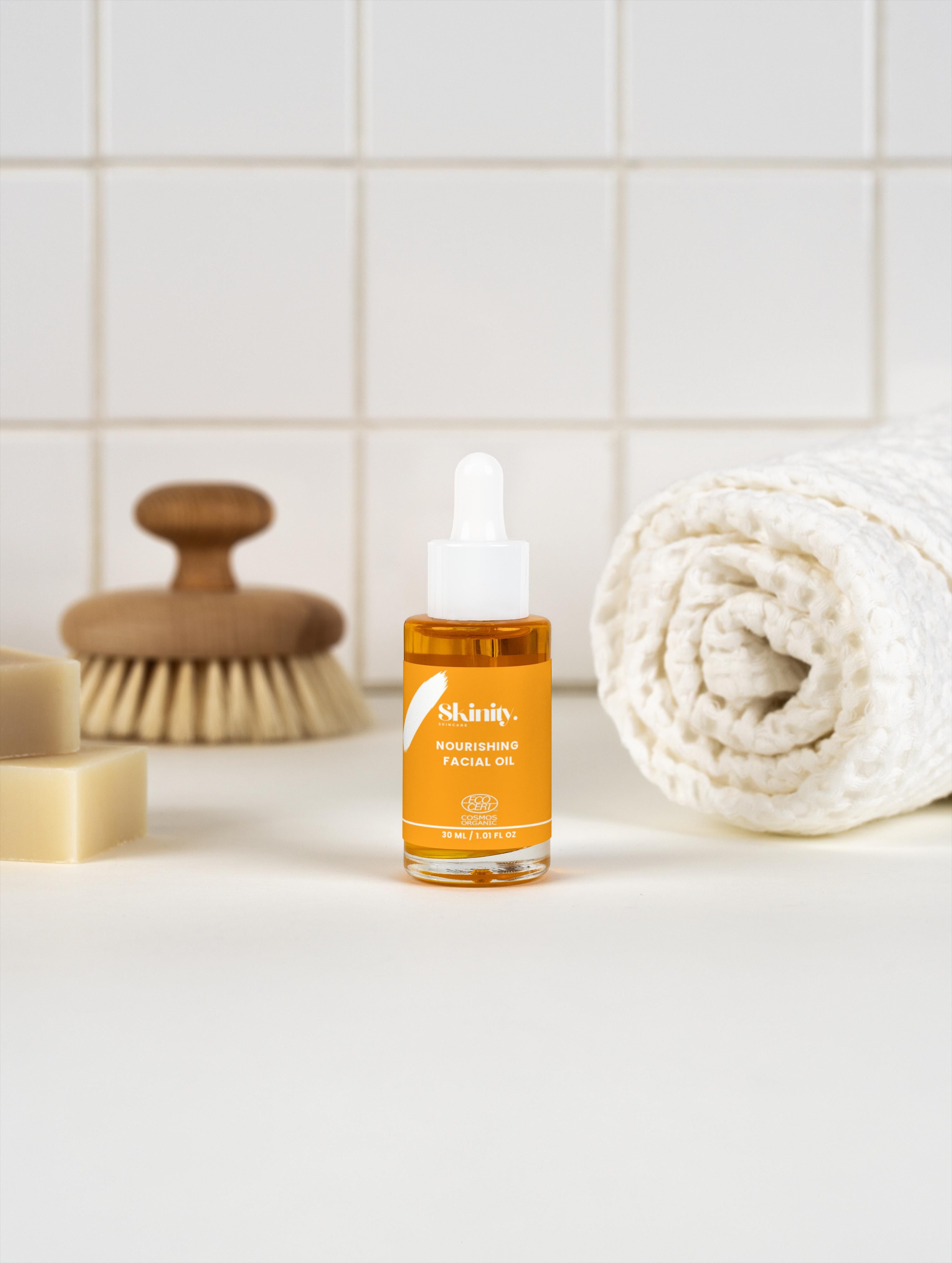 Nourishing Facial Oil For All Skin bottle on a bathroom countertop with brush and towels