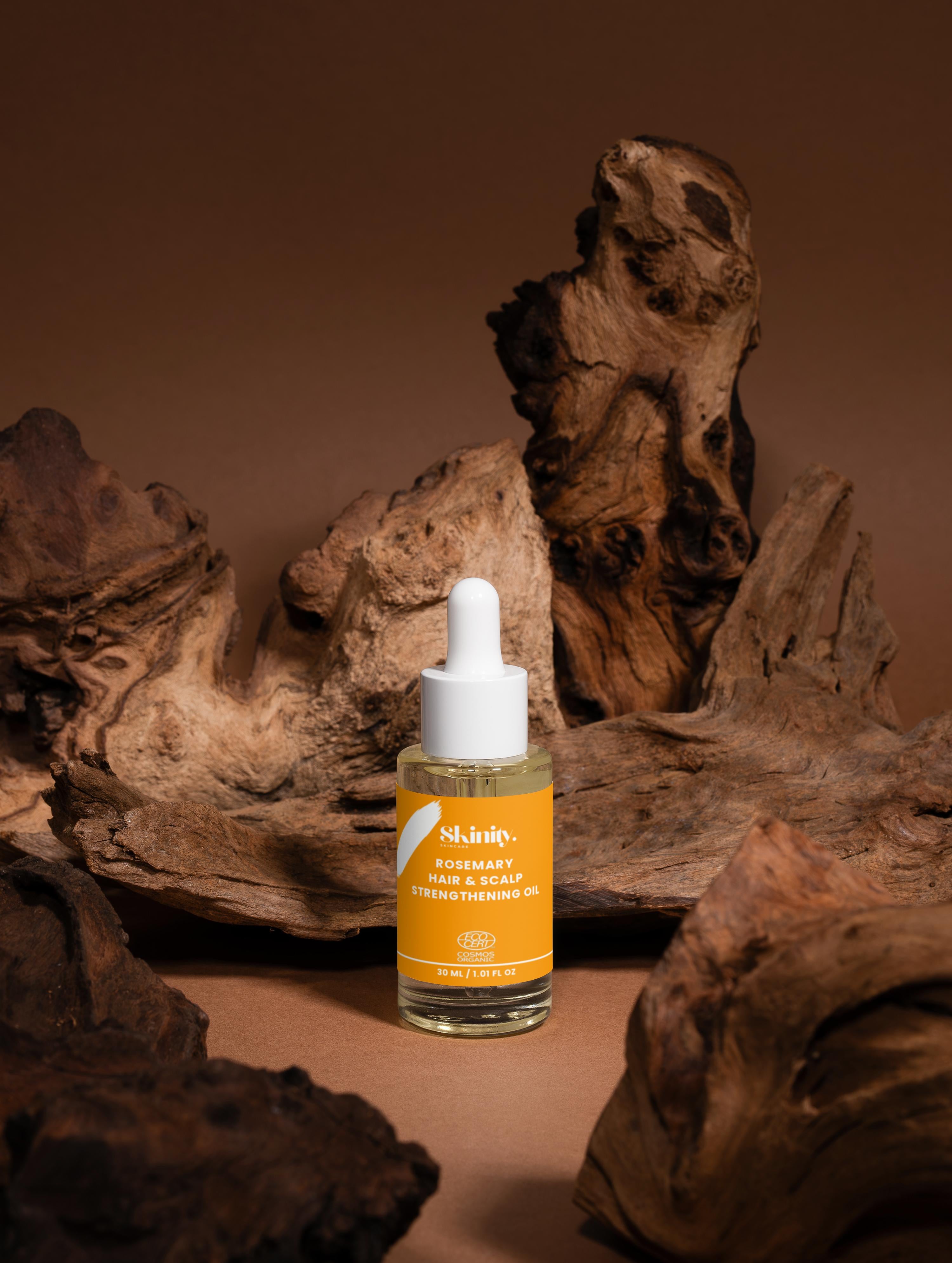 Rosemary Hair and Scalp Strengthening Oil bottle surrounded by natural wood decor.