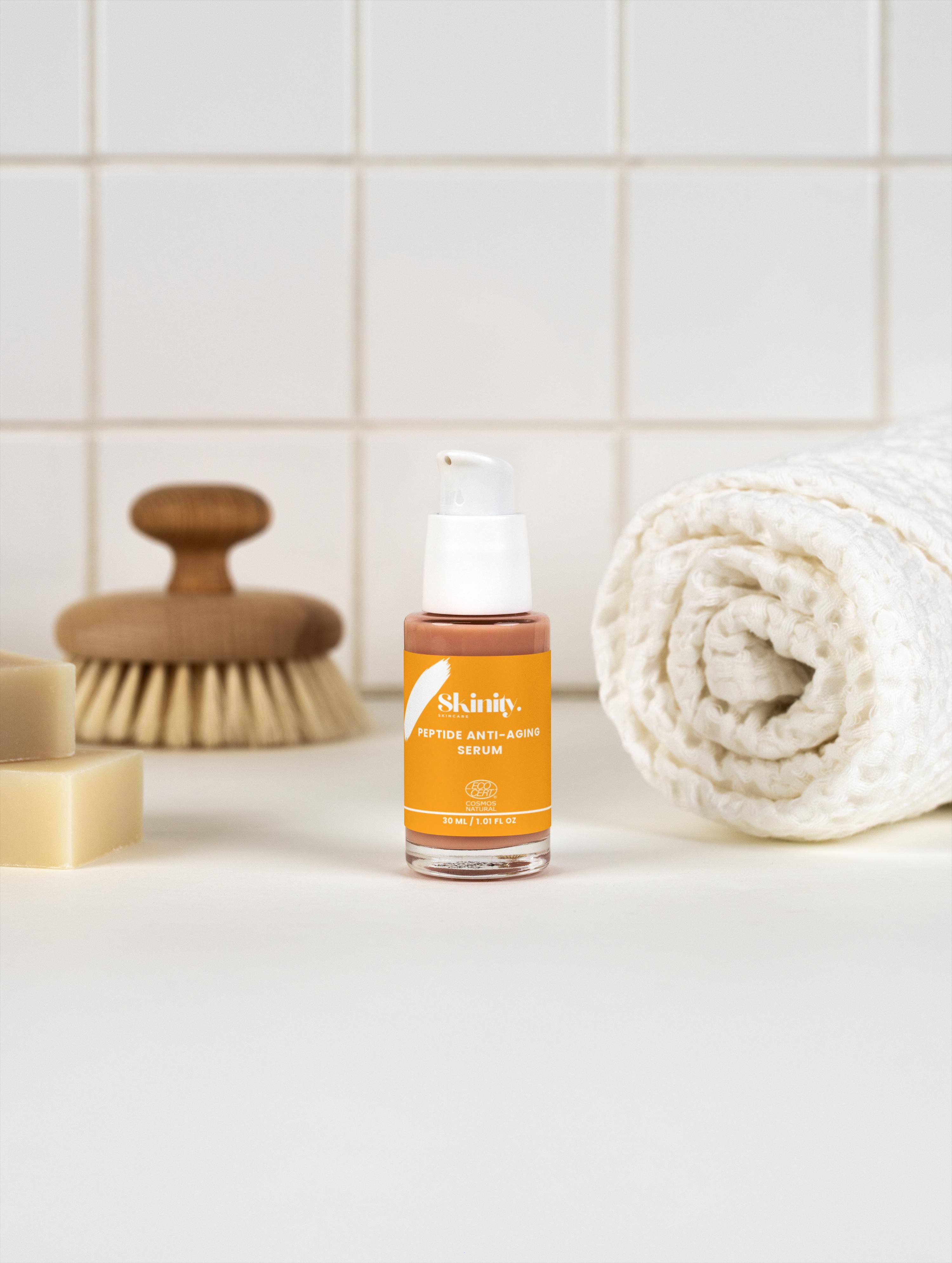 Peptide Anti-Aging Serum for All skin displayed with a bath brush and towel in a clean bathroom setting.