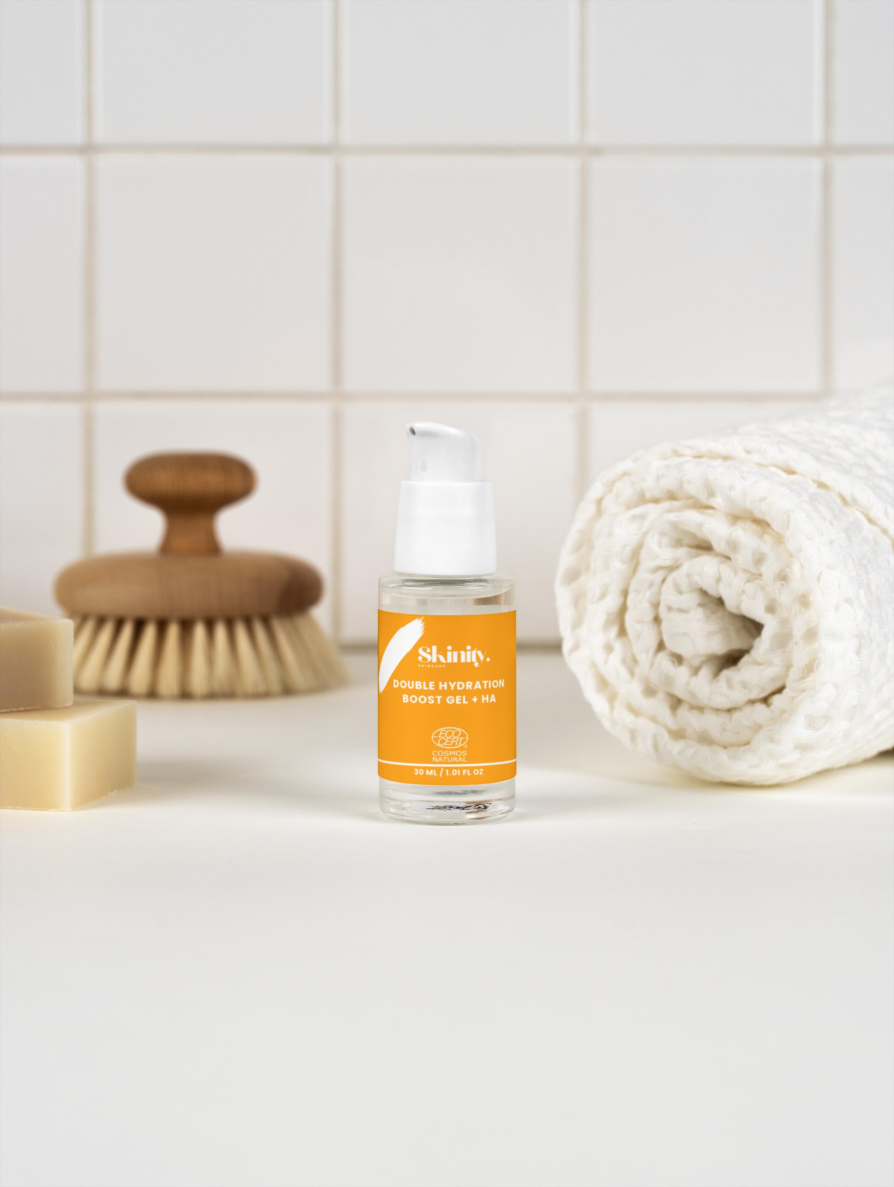 Double Hydration Boost Gel + HA placed beside a rolled towel and a wooden brush on a clean countertop.