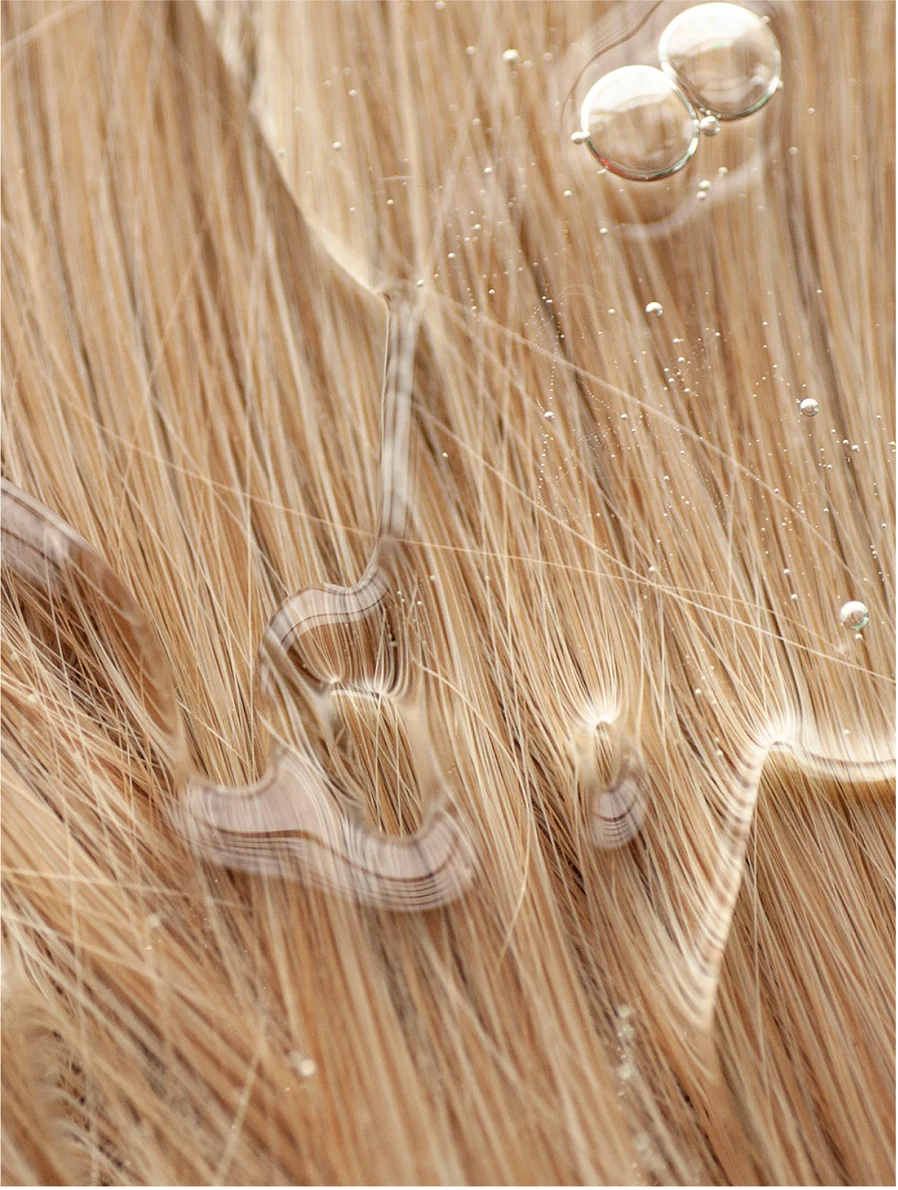 Close-up of shiny, healthy hair with water droplets, showcasing effects of Keratin Volume Boost Conditioner.