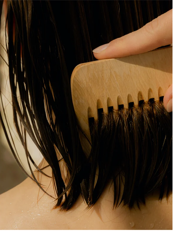 Applying Keratin Volume Boost Conditioner to smooth and detangle wet hair with a wooden comb.