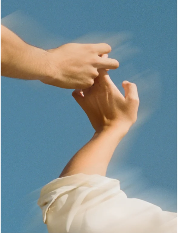 Two hands reaching out to each other against a blue sky, symbolizing connection and support.