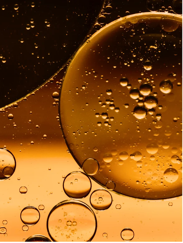 Close-up of golden oil droplets and bubbles, representing Omega 6-9 Glowing Skin Body Oil For All Skin Types.