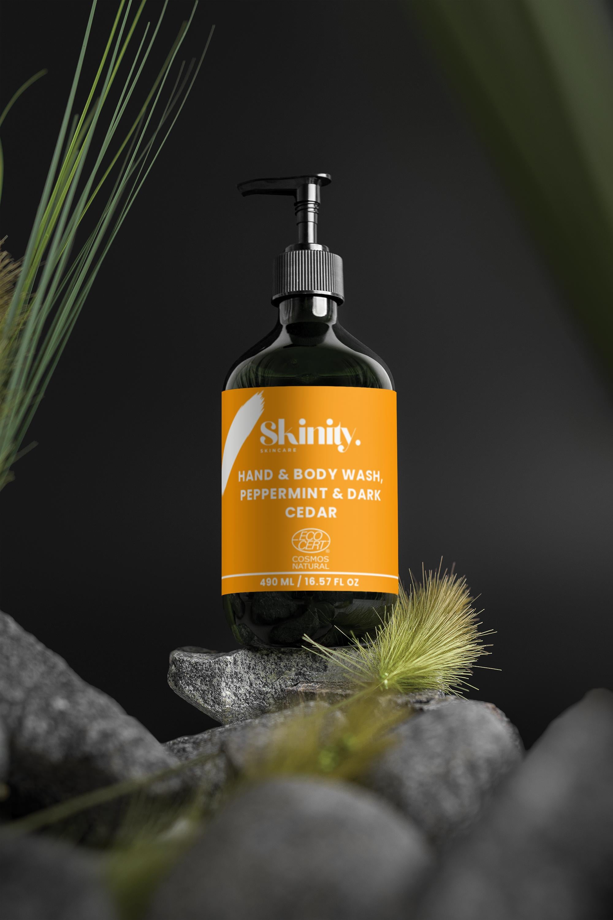 Hand and Body Wash Peppermint and Dark Cedar bottle displayed on rocks with plants in background.