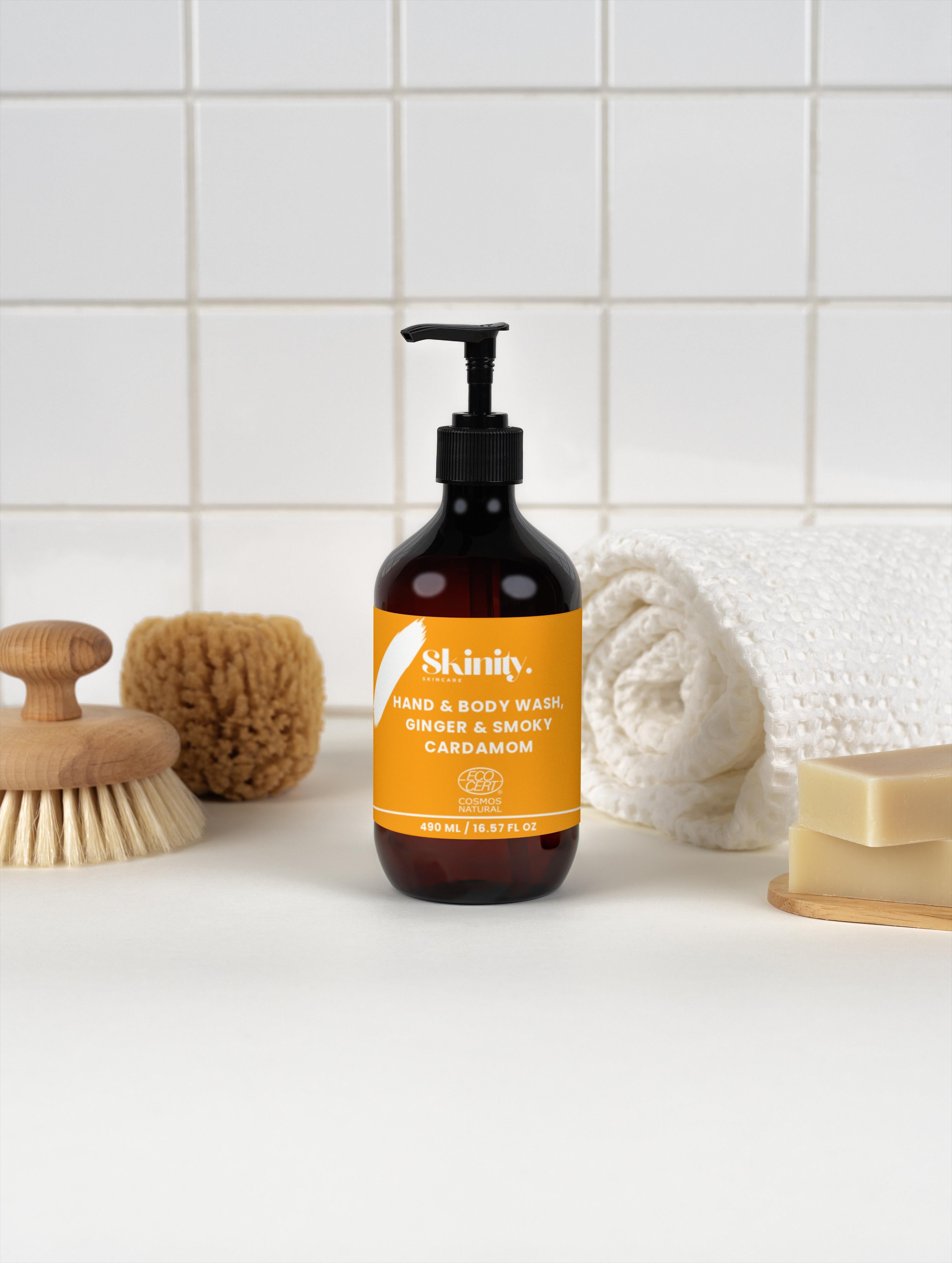 Hand and Body Wash Ginger and Smoky Cardamom bottle next to washcloth and bath accessories on a tiled background.