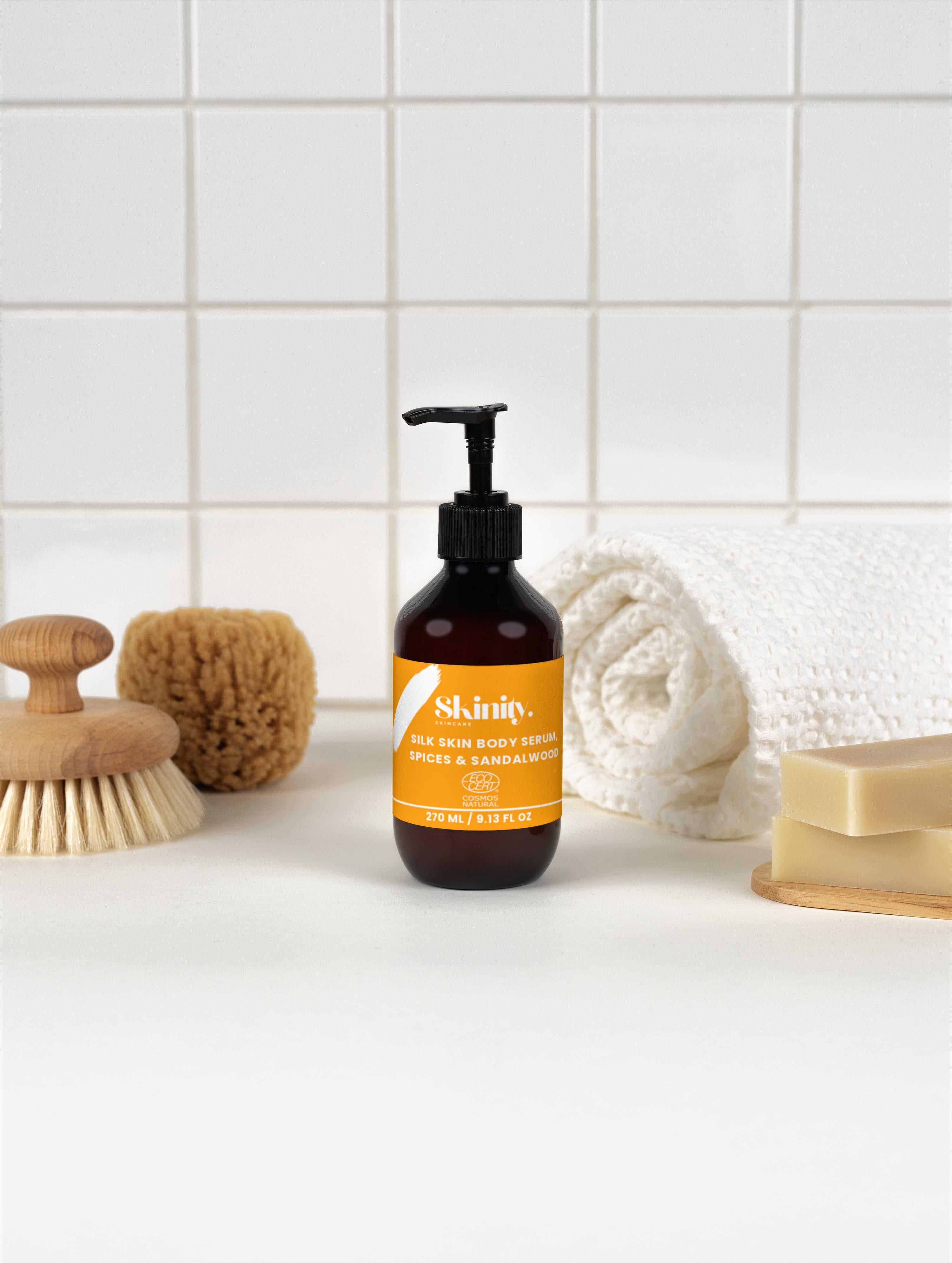 Silk Skin Body Serum Spices and Sandalwood bottle on bathroom counter with accessories and towels.