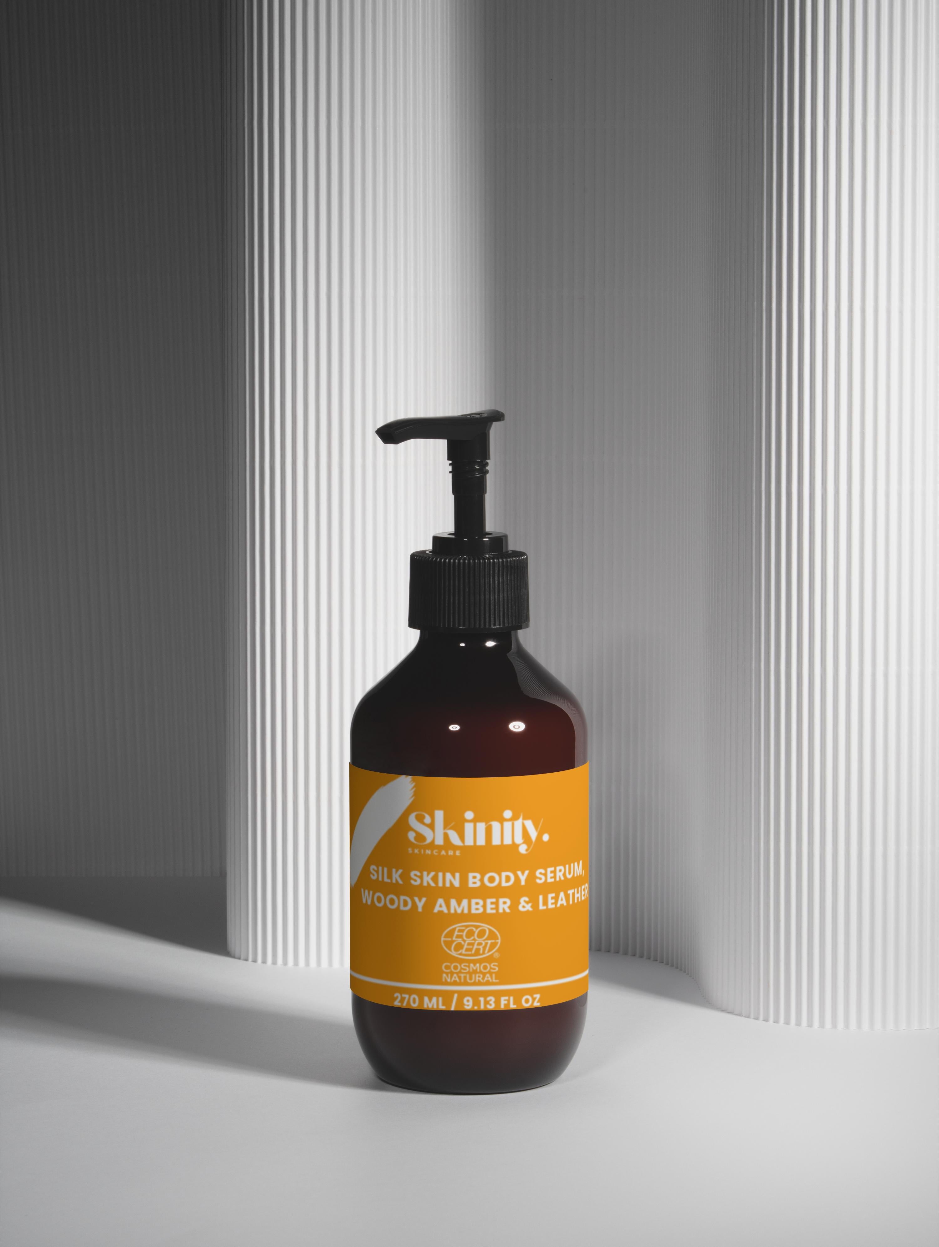 Silk Skin Body Serum Woody Amber and Leather in an elegant bottle on a textured background.