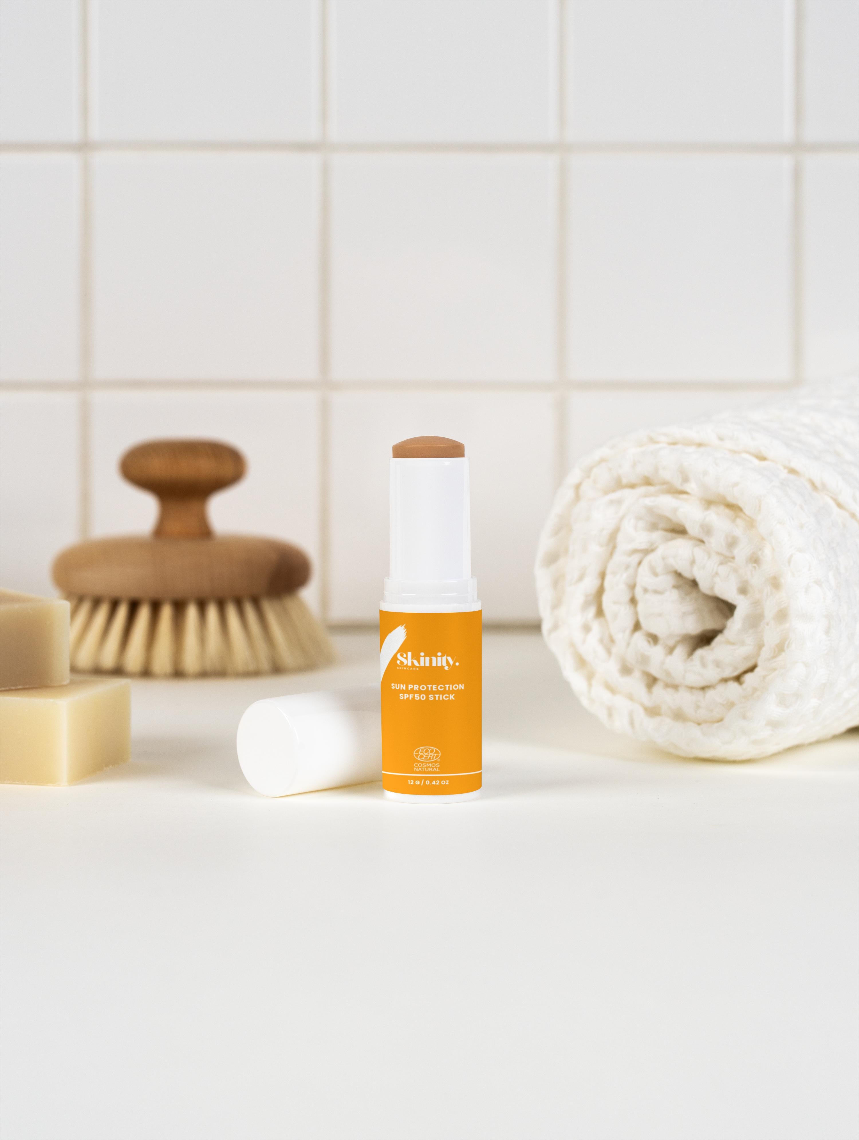 SPF 50 tinted sunscreen stick on a countertop with skincare products, perfect for all skin types.