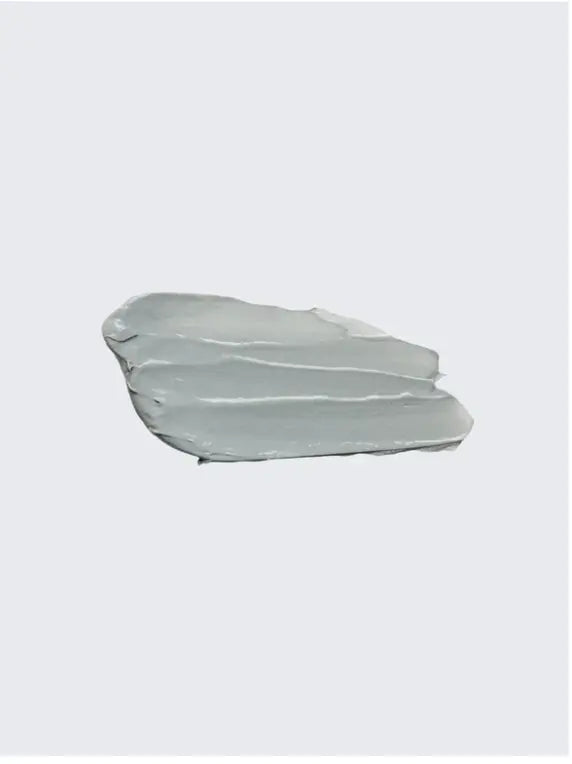 A thick, textured swipe of light gray cosmetic cream or gel on a solid light gray background.