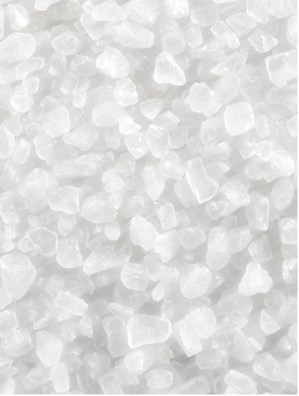 Macro close-up of white mineral crystals and sea salt particles on a white background, highlighting the natural exfoliating ingredients of the Skinity clay mask.