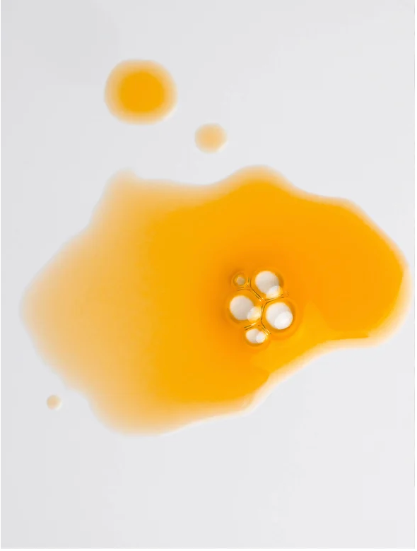 All-In-One Facial Oil for all skin, a luxurious product in a vibrant yellow oil drop on a white surface.