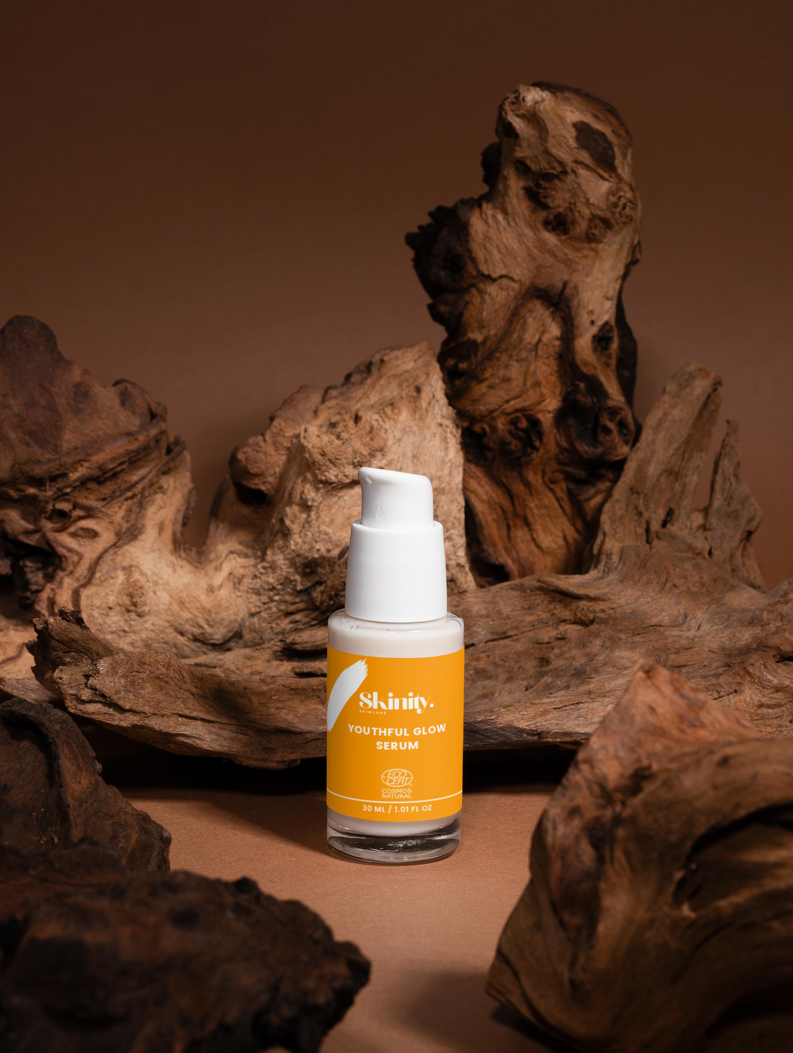 Youthful Glow Serum For All Skin Types in a stylish bottle on a wooden background.