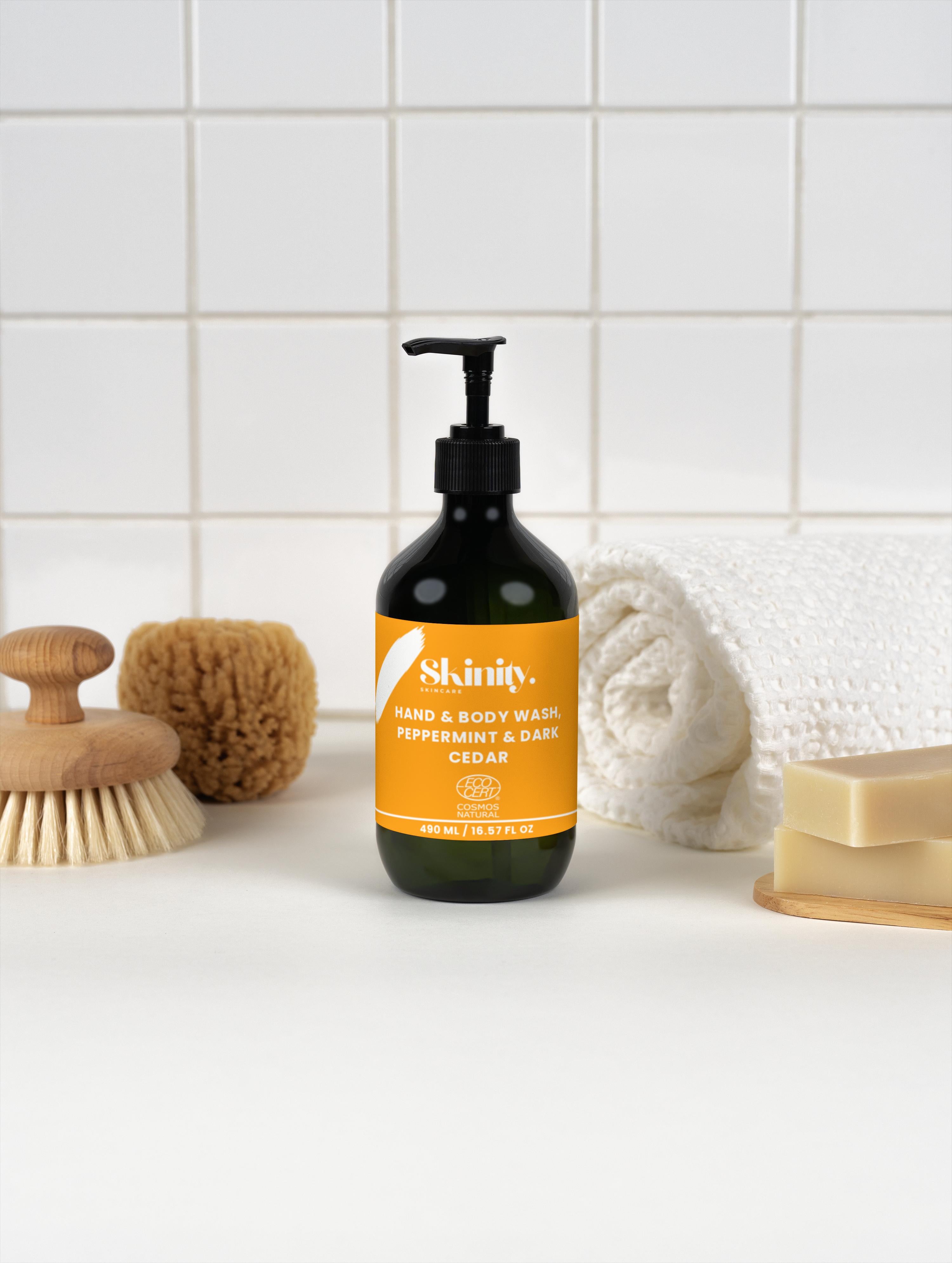 Hand and Body Wash Peppermint and Dark Cedar in a pump bottle, surrounded by bath accessories and towels.